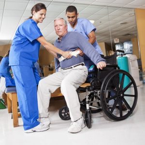 Physical therapists helping patient (60s) from treatment table into wheelchair.
